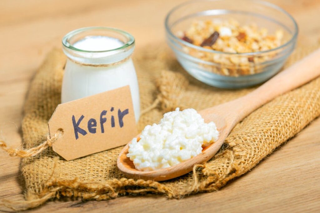 Un bicchiere di kefir accanto a chicchi di kefir su un tavolo di legno.
