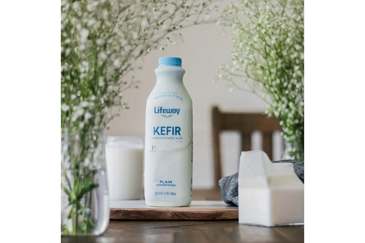 Bicchiere di kefir su un tavolo con cucchiaio e chicchi di kefir accanto.